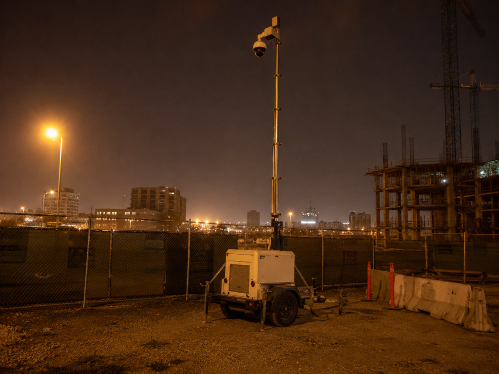 Security camera mounted on a pole overlooking an Oakland construction site at dusk with a tower crane in the background.