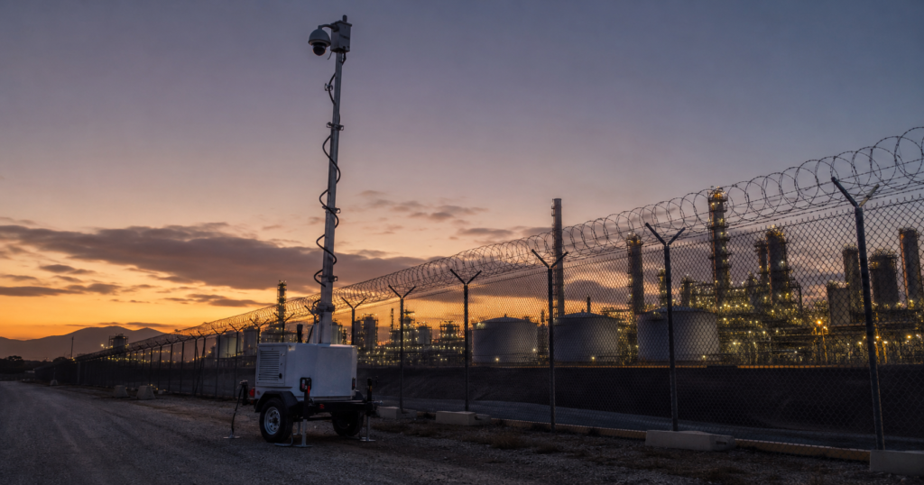 California industrial plant outer perimeter with mobile surveillance trailer monitoring fence line at twilight