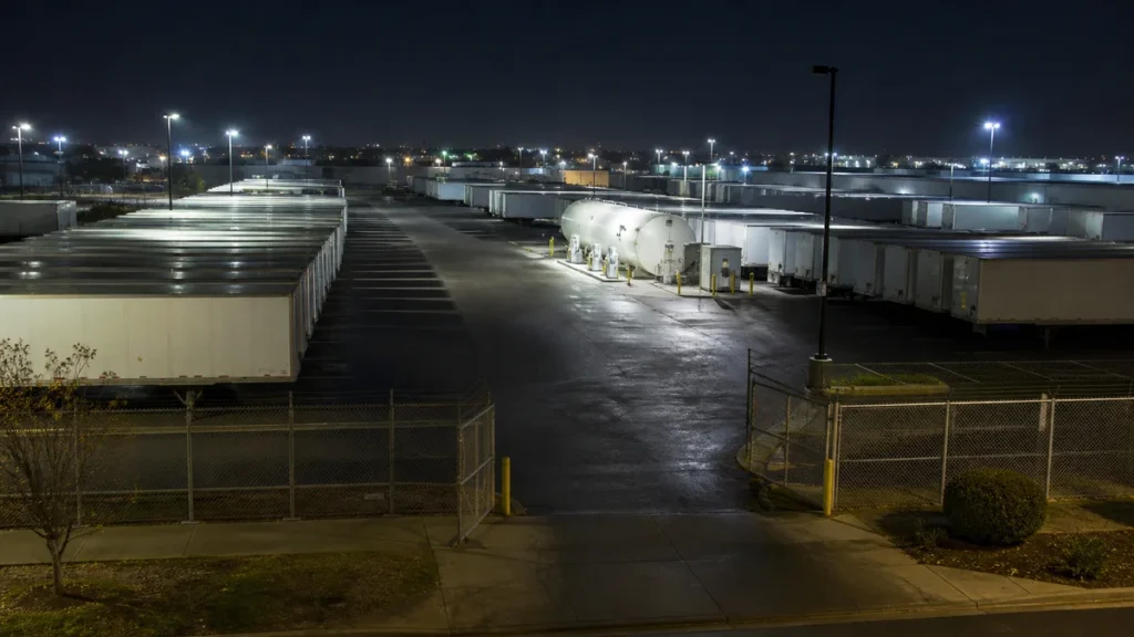 Rows of parked semi trailers and a fuel island in a fenced truck yard lit at night